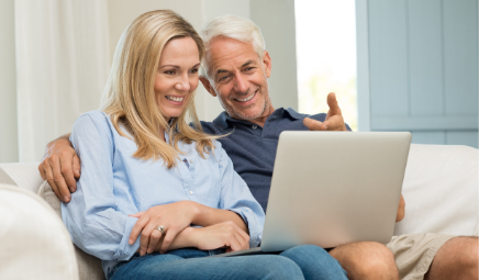 Smiling couple sitting on a white couch with laptop