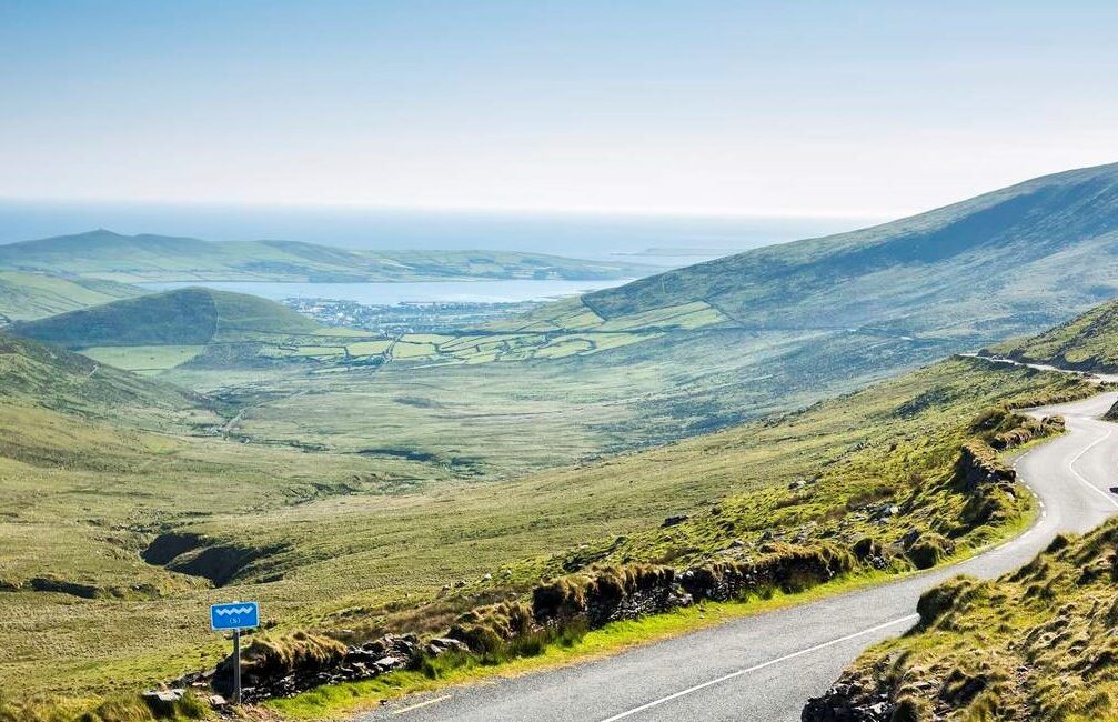 Empty hillside road with a backdrop of green hills and the sea