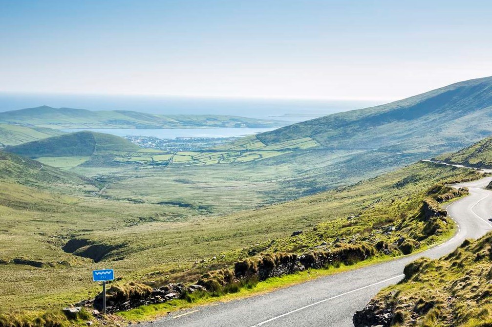 Empty hillside road with a backdrop of green hills and the sea